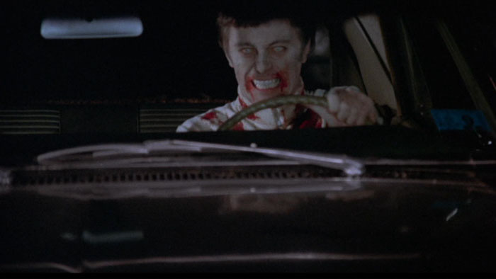 Undead soldier with blood on his face drives a car with a menacing grin in a scene from Dead of Night (1974).