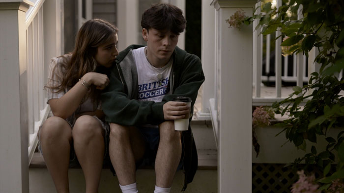 Young woman comforts a troubled young man holding a coffee cup on a porch step.