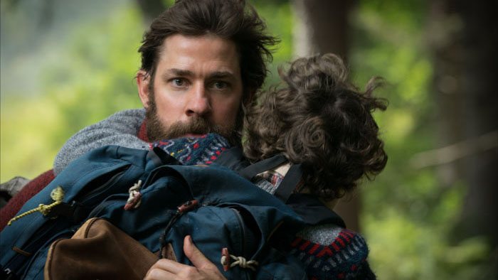 John Krasinski holding his child in a tense forest moment from the horror-thriller A Quiet Place