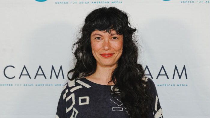 Filmmaker Angeline Gragasin smiles at a CAAMFest event, standing in front of a Center for Asian American Media backdrop