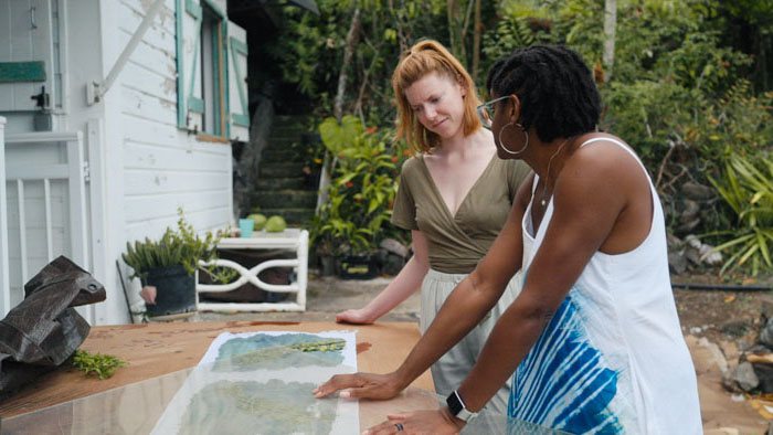 Two women examining artwork outdoors in tropical setting