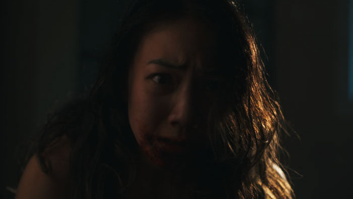 Close-up of a blood-smeared woman staring in fear in Bleeding.