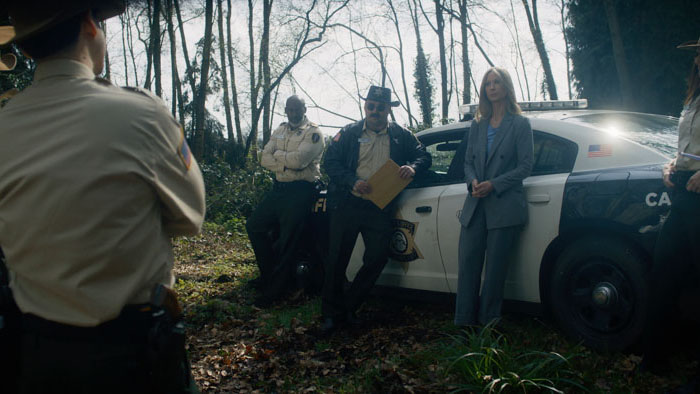 Sheriff’s deputies gather outside a patrol car in a wooded area in a scene from Bogieville.