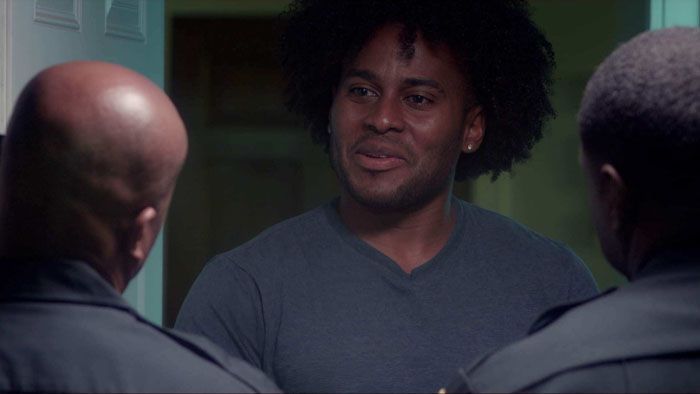 Man speaking to two police officers in a tense scene from Finding Nicole