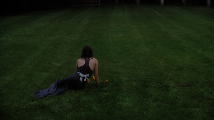 Grace lies alone in a dark dress on a vast green lawn in Fractals