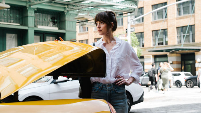Dakota Johnson stands beside a yellow cab in New York City in The Materialists