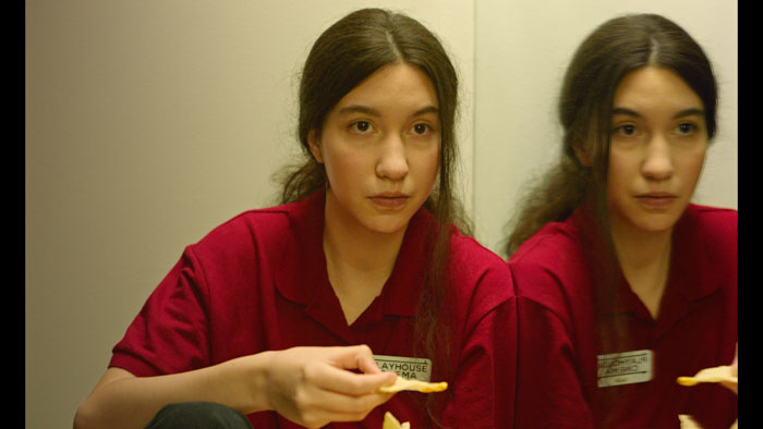 Teen girl in red uniform eats nachos in front of a mirror
