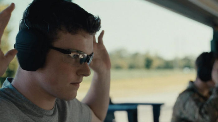 Teen boy wearing safety glasses and earmuffs prepares to shoot at outdoor range