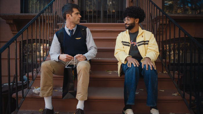 Simon and Bruce sit together on a brownstone stoop in The Travel Companion.