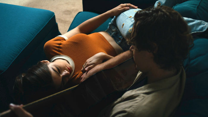 Catharine Daddario lies on a couch while Sky Nelson plays guitar beside her in The Tributaries