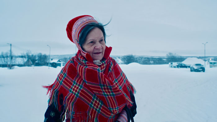 Elder Sami woman in traditional dress stands against a snowy landscape in The Tundra Within Me