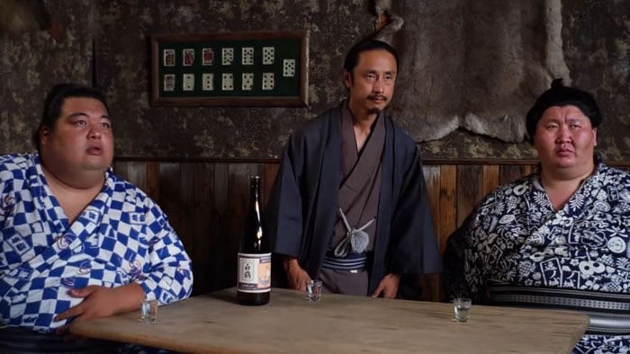 Scene from The Wide West with Hiroki Sumi, Ichi, and a Japanese delegate seated at a saloon table
