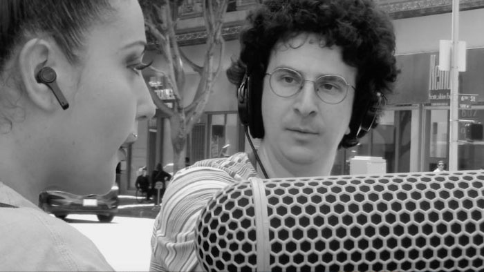 Andrew records audio with a large boom mic while Christie speaks in Tricks Can Go Wrong.