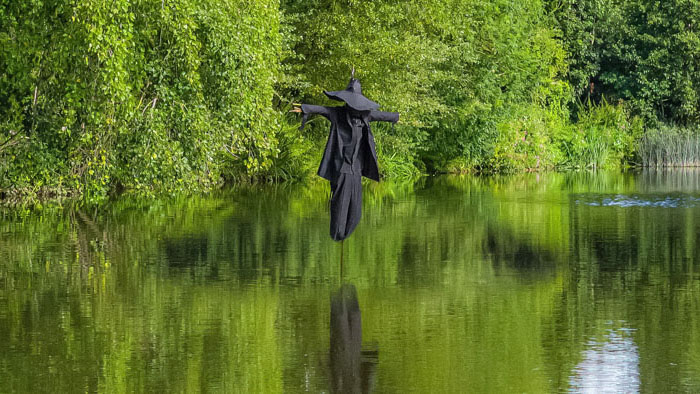 A haunting scarecrow in a witch’s hat stands eerily over a river in Wild Swimmers