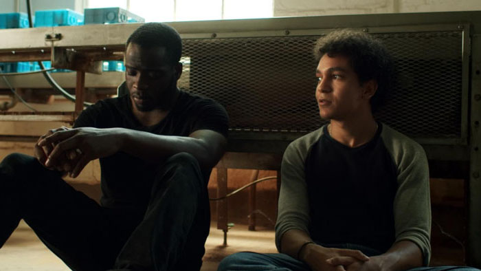 Two men sit on a factory floor, deep in conversation in Without Morals