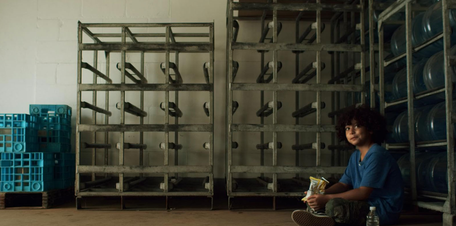 Young boy sits alone on a warehouse floor holding snacks in Without Morals