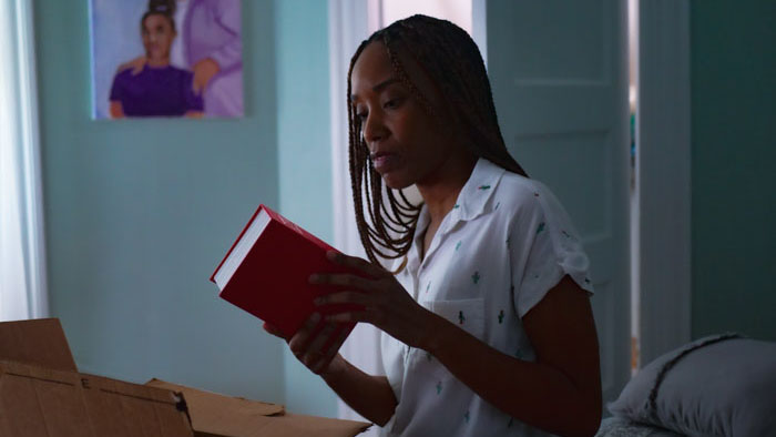 Abbie holds a red book while unpacking boxes in her childhood bedroom in Myth of the Ghost Kingdom.