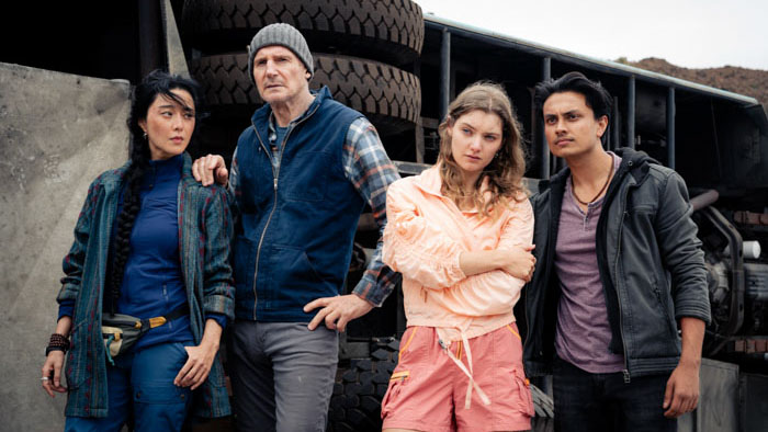 Liam Neeson and cast in Ice Road: Vengeance standing in front of an overturned truck