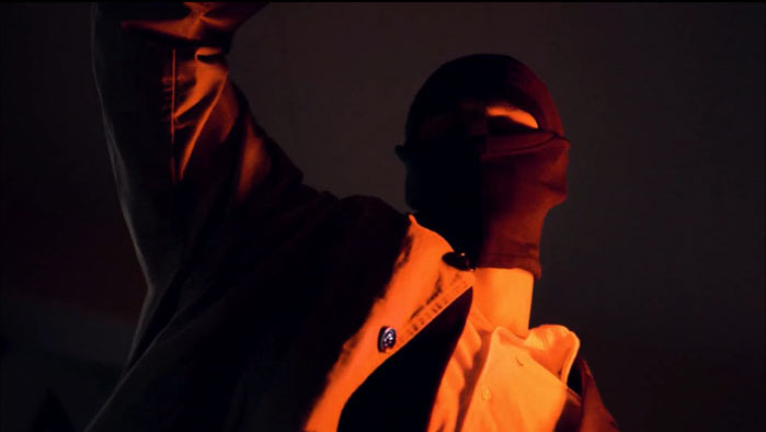 A masked figure shrouded in shadow and orange light, from the short film Numbers (Liczby).