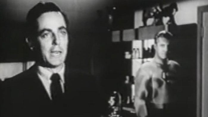 Man in suit speaks as Superman stands in background in Stamp Day for Superman