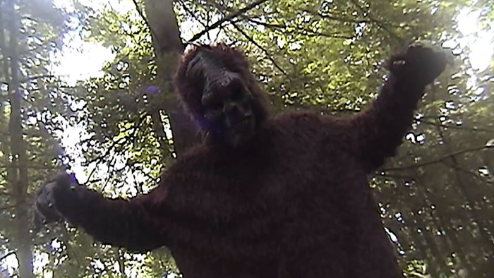 Man in a Bigfoot costume raises his arms in a forest scene from The Haunting of Prince Dom PedroTitle: Bigfoot in the Woods – The Haunting of Prince Dom Pedro