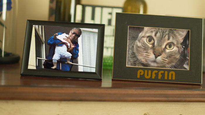 Framed photo of a man dangling a baby next to a framed photo of a tabby cat labeled "Puffin"