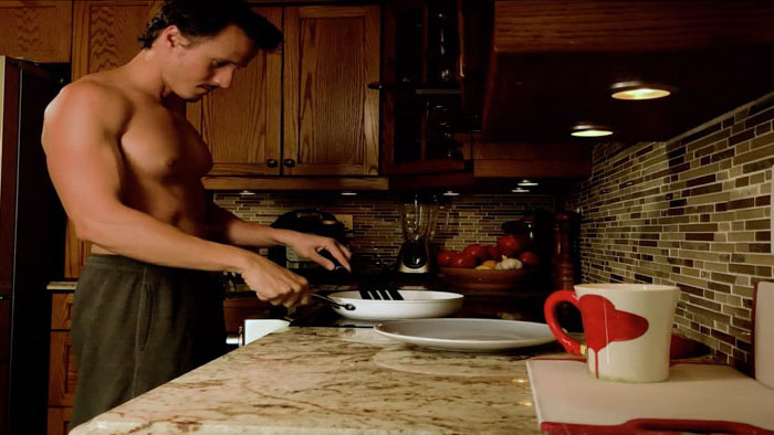 Shirtless man cooking breakfast in a kitchen scene from It Rained That Morning
