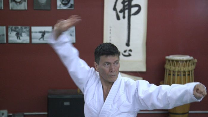 A martial arts instructor in a white gi performs a kata in a dojo