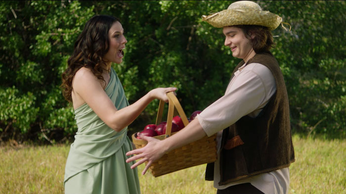 Demi smiles as Zip hands her a basket of apples in a sunny field