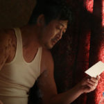 Text: Kim Yoon-seok as Father Kim examining a photograph in The Priests