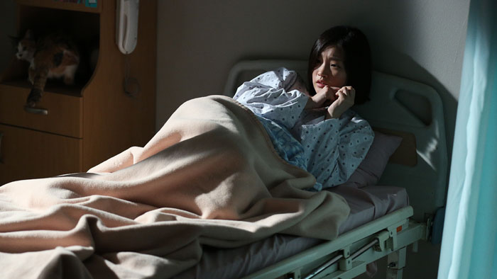 Park So-dam as Young-shin lying in a hospital bed in The Priests