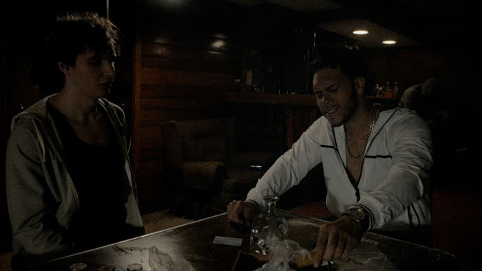 Two men sit at a dimly lit table in a tense scene from Death’s Sonata.