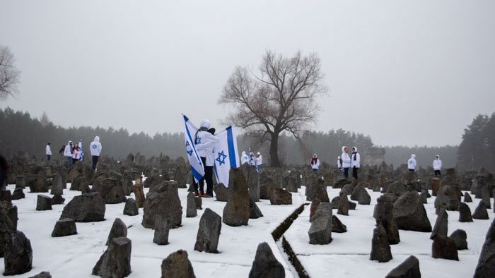 Israeli students stand with flags among memorial stones at a Holocaust site in Delegation.