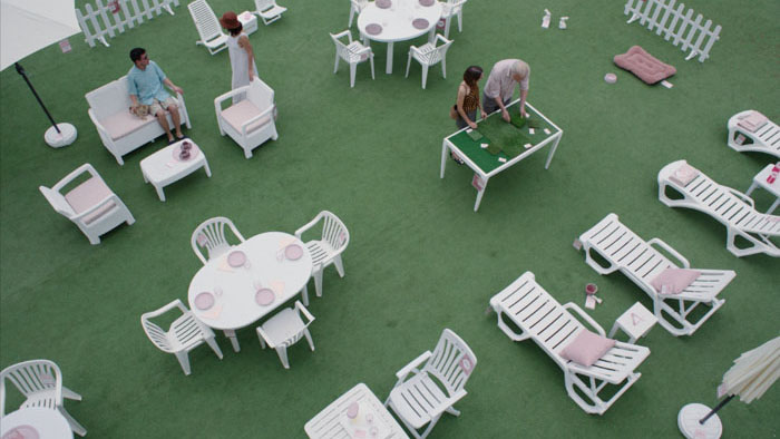 Scene from Forastera showing people in a white plastic outdoor café setting on green turf.