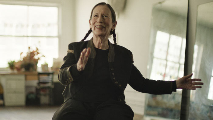Meredith Monk smiling and gesturing during an interview in Monk In Pieces.