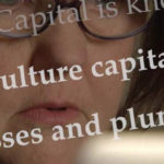 Close-up of a journalist’s face with the words “vulture capitalism” projected across the screen.