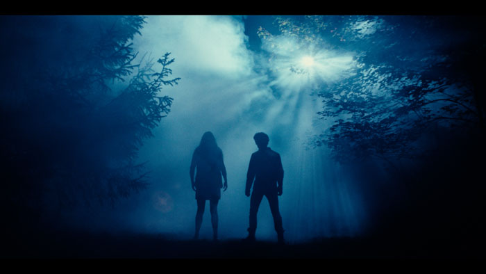 Two figures stand in a foggy blue-lit forest in Bloodsuckers and the Grimoire.