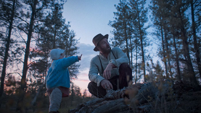 Robert Grainier with his young child in the forest at dusk in Train Dreams