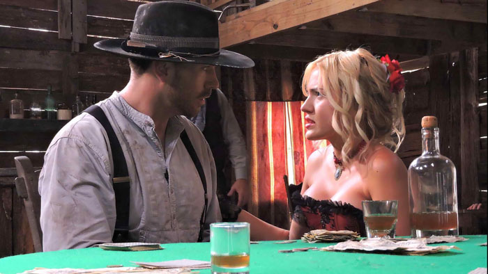 Silas and Rose sit at a saloon table in a tense moment from A Gunfighter’s Deal.