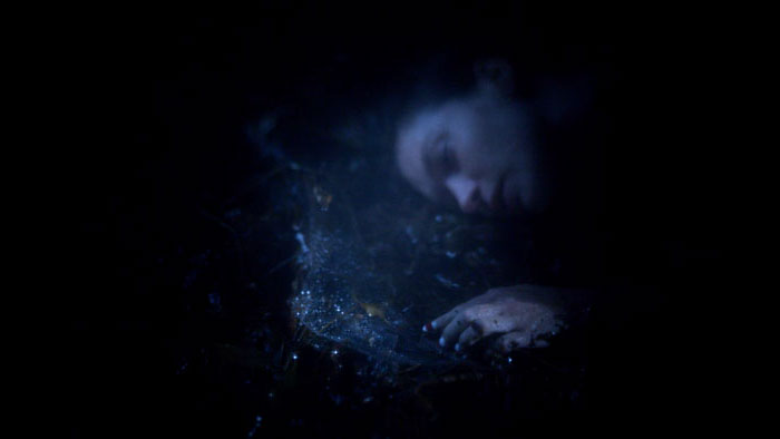 Two women kneeling in a field at sunset, facing each other with soft backlighting.