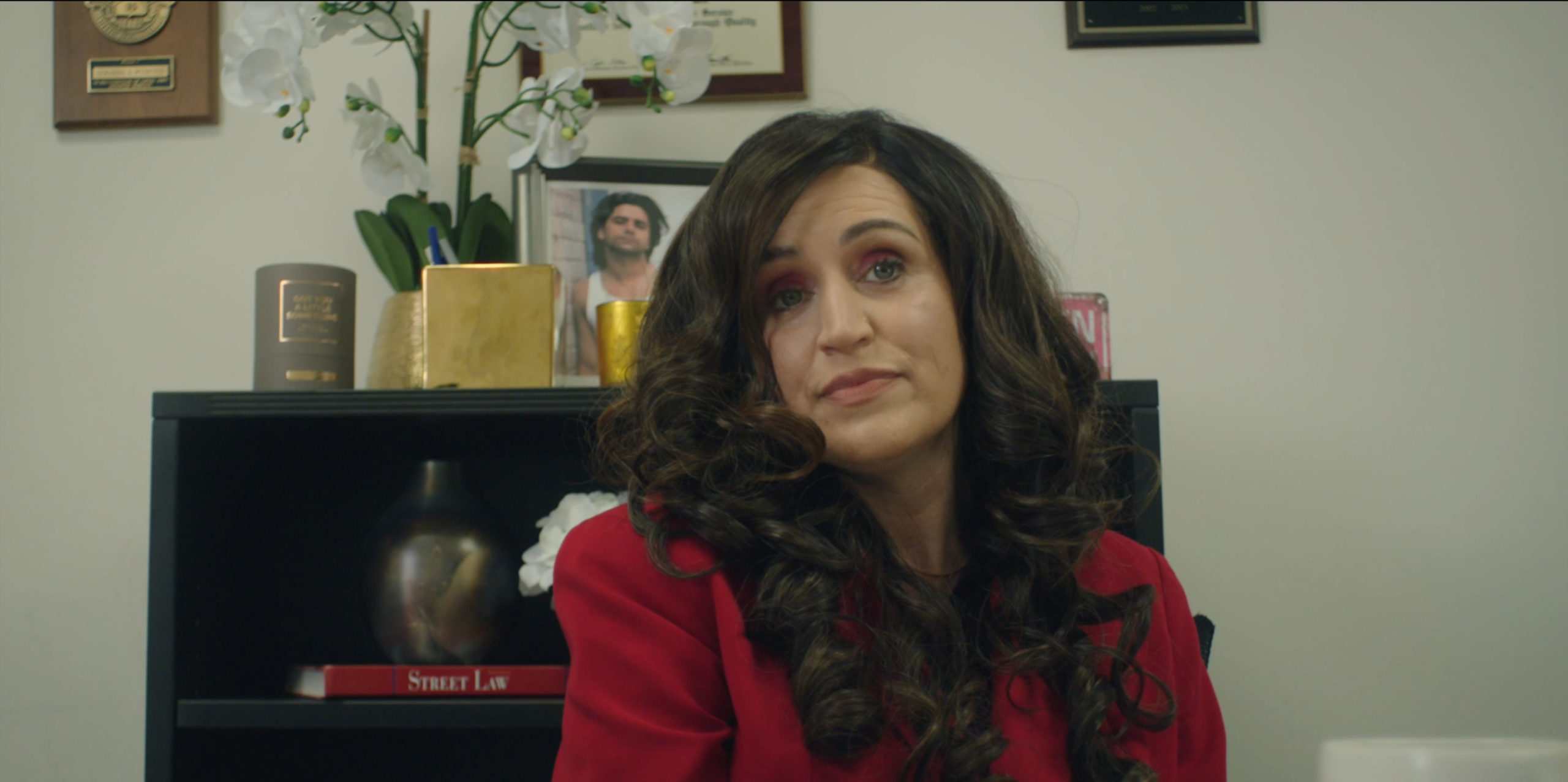 Janine’s boss sits behind her desk, expressing concern about Janine’s attendance in Blowing Up.