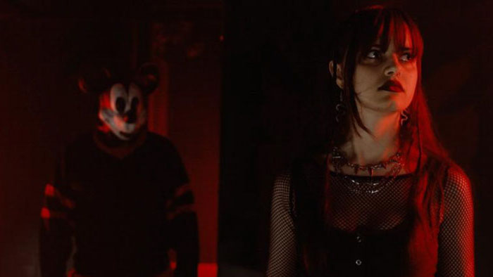 Rebecca stands in red light unaware of the Mickey Mouse–masked killer behind her in The Mouse Trap.