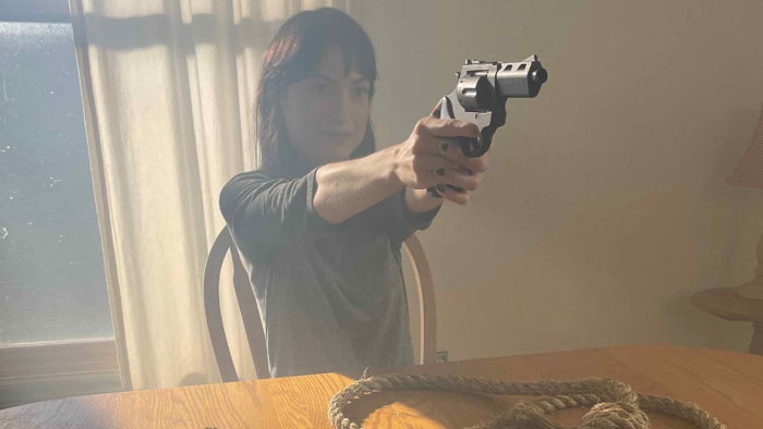 Debbie aims a revolver while seated at a table in Half Dead Fred