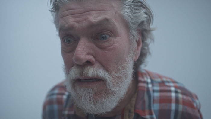 Colin Ward as Herman in Herman (2025), close-up of the isolated recluse in his cabin.