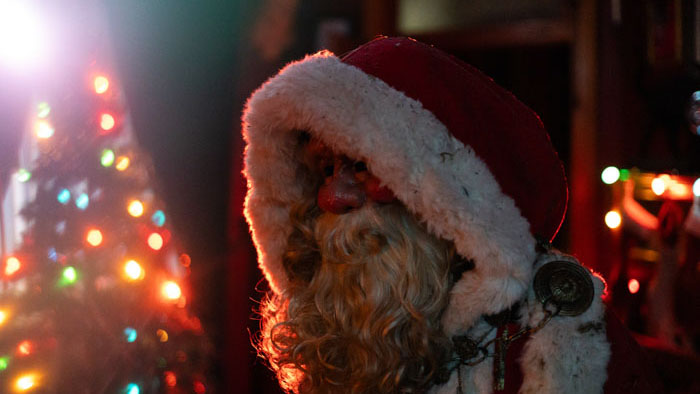 A dimly lit Santa figure stands beside a glowing Christmas tree in The Specter of Christmas. 