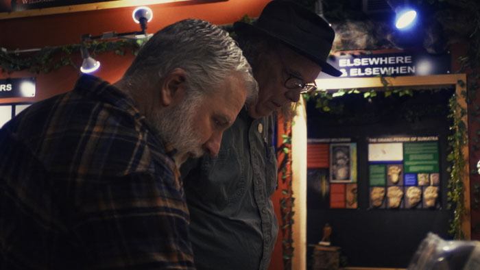 Two researchers review materials indoors while discussing the Ape Canyon Bigfoot legend in The Siege of Ape Canyon (2025). 