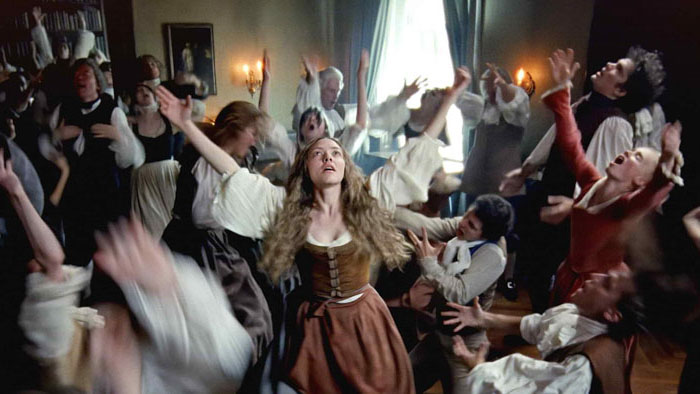A period room erupts into ecstatic worship as a young woman raises her arms while Shaker followers dance around her.