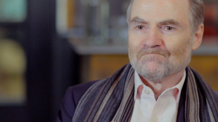 Documentary interviewee in close-up wearing a scarf, speaking on camera.