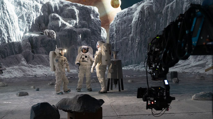 Behind-the-scenes photo of three actors in spacesuits on an icy set as a large camera rig films a scene for Europa (2025).