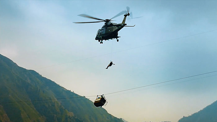 Helicopter rescue operation above a damaged cable car dangling over a mountain valley in Hanging by a Wire (2026).